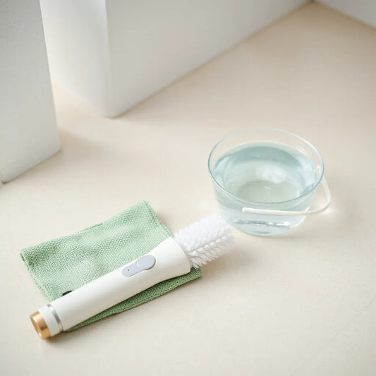 Rechargeable cordless cleaning brush with soft bristles on a clean floor near soapy water and a microfiber cloth